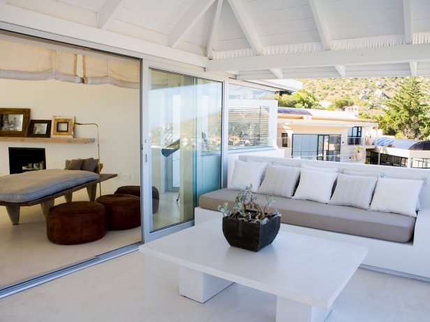 Veranda and living room with sliding glass door wall leading outside to this white furniture and table design under an awning. 