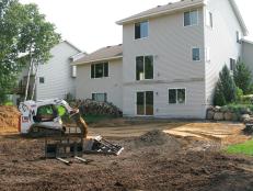 A person in a bobcat getting the ground ready planning for building a backyard patio on the back of the house.