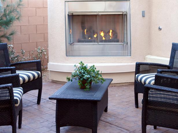A gas fireplace in an outdoor living room with black wicker furniture.
