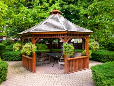 A paver patio with a beautiful wood gazebo situated in a garden.