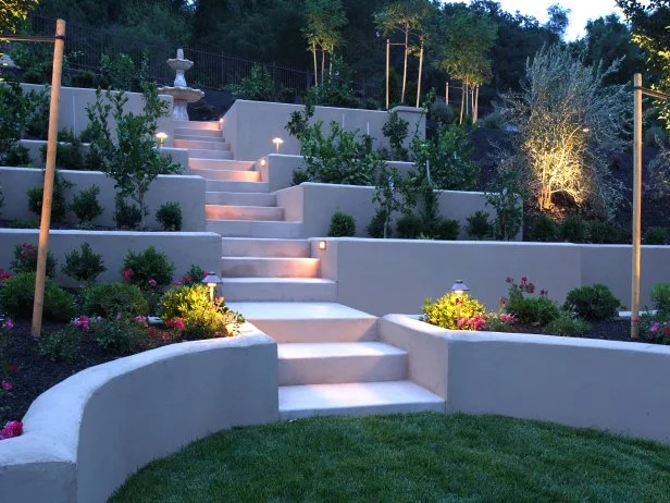 A luxury backyard that is beautifully lit and hardscaped with concrete structure and steps. 