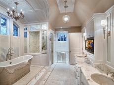 A pedestal tub, marble and basketweave tile, and high ceilings add drama to this spacious bath, which comes complete with a flat panel TV on an adjustable mount for total relaxation.