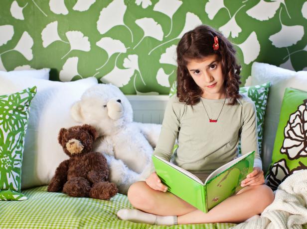 Girl Sits on Her Comfy Daybed in a Green and White Bedroom 