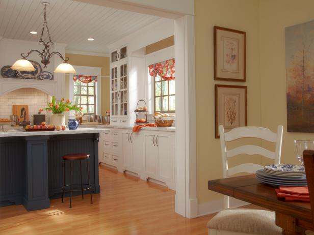 Neutral Kitchen With Navy Island Opens to Yellow Dining Room