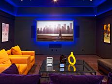 Sitting areas with colorful furniture on a hardwood floor and large flat screen tv with neon ceiling and wall.