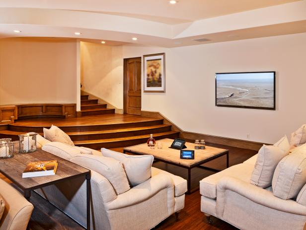 Living area with flat screen mounted on the wall with white furniture, wood coffee table, hardwood floor and steps leading up to other rooms. 