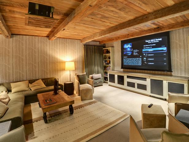 Rustic media room with wood ceiling and beams, large flat screen, rustic table, rug, and comfy seating. 