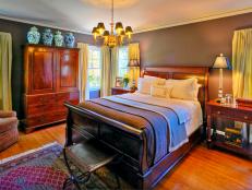 Traditional bedroom with wood furniture, hardwood floor and rug, side tables with lamps, and sitting area. 