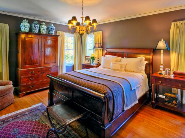 Traditional bedroom with wood furniture, hardwood floor and rug, side tables with lamps, and sitting area. 