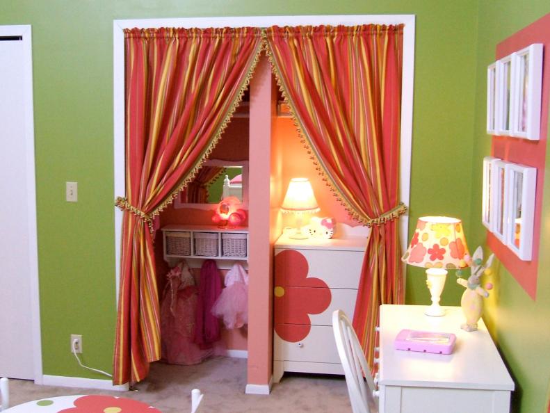 Green and orange girls bedroom with orange striped curtains in a storage closet area for kids items, white desk with chair and floral lamp shade, floral decor, and green wall. Design by RMS user gogirlgo
