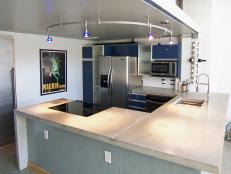 Concrete kitchen countertop with track lighting, and a light green base with an industrial type design. 