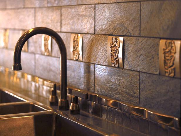 A bronze metal tile backsplash with decorative pieces behind a faucet and sink. 