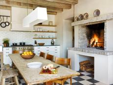 A wood-burning fireplace designed for cooking adds Mediterranean charm to this eat-in kitchen. The communal farm table is the centerpiece of the space. A modern light fixture provides a foil for the rough-hewn ceiling beams.