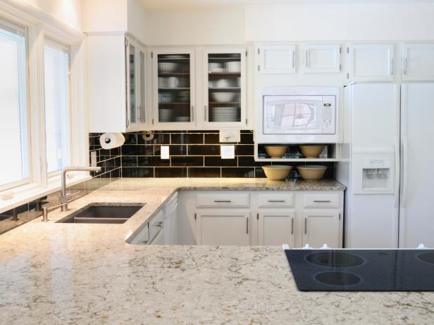 Modern Kitchen with white granite countertops and white kitchen cabinets, black tiled backsplash. 