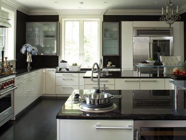 Wide view of a black and white kitchen with white cabinets, dark countertops, clean design, see through cabinet doors, and kitchen island. 