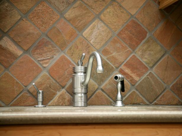 A tight shot of slate tile backsplash behind the faucet and sink in the kitchen of a contemporary home.