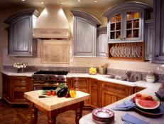 This shows different kitchen cabinet options. Darker base cabinets ground the space while the soft-gray finish on upper cabinets highlights their unique shape (Design by Didier Michot).