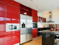 A modern kitchen with stainless steel applaiances and red, black, and glass european style cabinets. 