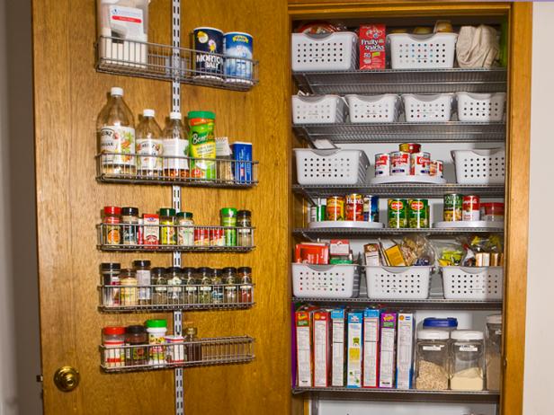 A wide shot of a pantry full with grocery items and white baskets. The pantry door has a door rack organizer on it.