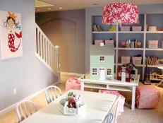 Playroom in the basement area with red lamp shade, kids table with craft tools, mermaid artwork, and playhouses. 
