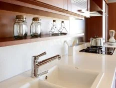 Side view of a white kitchen with red wood shelving, white countertop, modern interior design. 