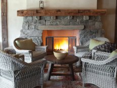 Four wicker armchairs surround an antique pine table in the downstairs recreation room. The fireplace mantel is an antique barn beam. 