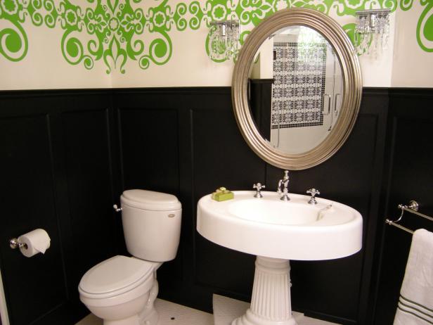 Wide view of bathroom with small round sink area on a pedestal, round mirror on a green wall mural, black wainscoting, and towel holder.                                