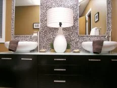 Dark vanity area with updated design, above counter sinks, lamp, dual mirrors, circular design wallpaper, and countertop decor. 