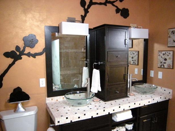 Wide view of newly renovated bathroom with floral artwork stretched across the warm toned wall, tiled countertop, vanity, dark wood cabinetry, and double mirros and glass sink bowls. 