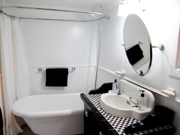 Black and white checkered vanity countertop, above ground tub, white modern style sink, round mirror, wainscoting around the wall and a clean design.