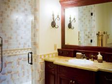 Pale yellow and cream tile and paint line the walls surrounding this cherry wood bathroom vanity. A large mirror and granite countertop add sophistication to this statement bathroom piece.