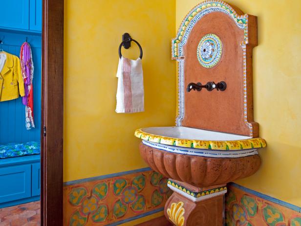 This powder room is inspired by Mediterranean design, with colorful walls, a clay pedestal sink, and a wrought iron pendant light and hand towel holder.