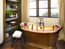 Cozy hideaway bathing nook with shimmering copper tub.  Spanish tile gives a rustic feel with subtle recessed lighting above.  A built-in shelf is within reach of the pedestal tub to hold everything needed for a relaxing bathtime.