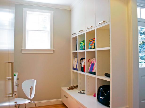 A white, open-faced cabinet unit has been placed along one wall in this mudroom, which also has a small desk, white chair, and pantry.