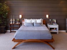 This cherry wood bed delivers clean, modern lines, particularly in the curved support at the foot. Linens in shades of blue and gray allow the wooden frame to stand out against the darker tones of the space. Design by Erica Islas.