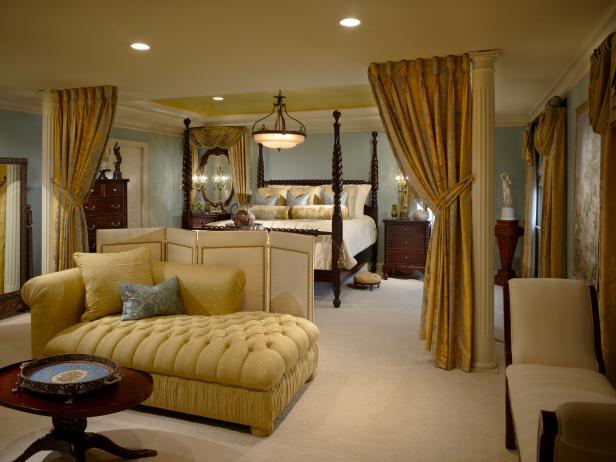 This elegant master bedroom features columns with tieback draperies to separate the sleeping area from the sitting room. A custom floor screen diffuses the hydraulic TV cabinet facing the four-poster bed. The curtain on the left side of the bed surrounds a mirror instead of a window to open up the space.