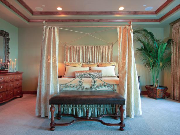 Sage green walls provide a relaxing back drop to this bedroom. Plush fabrics were used for the custom bedding ensemble. The fabric panels hanging on the bed frame create a romantic cocoon. Designer tip: Paint the wall color up on to a portion of the recessed ceiling to give the illusion of more height.