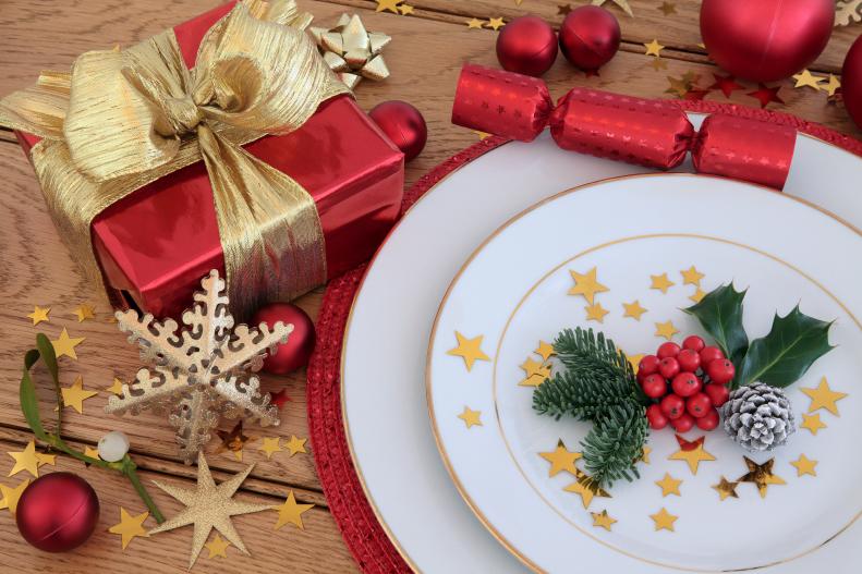 Christmas holiday dinner place setting with plates, gift box, bauble decorations, holly and mistletoe over oak table  background.