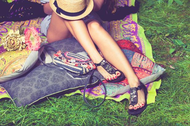 woman feet on grass in flat summer sandals lean on pillows  hat lay on legs from above