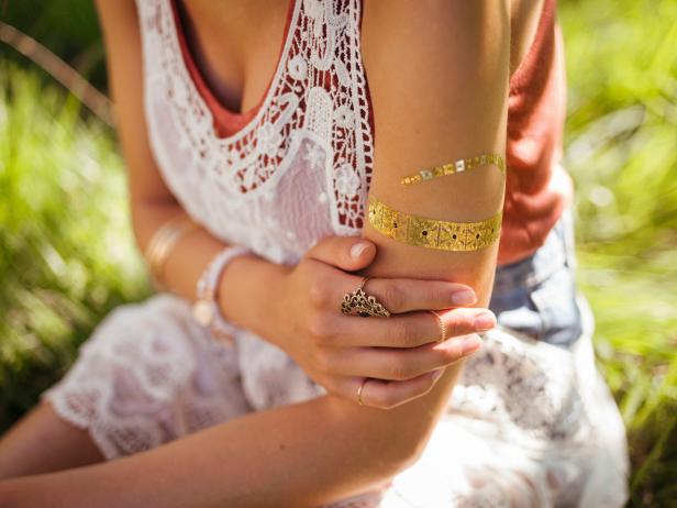 Cropped closeup of a girl in boho styled clothes with a temporary gold foil tattoo on her arm