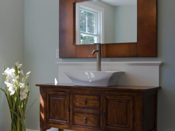 Transitional gray bathroom with antique vanity and wood mirror. 
