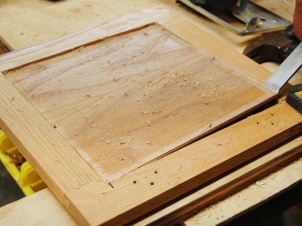 Prying a wood panel from a kitchen cabinet frame with a chisel.