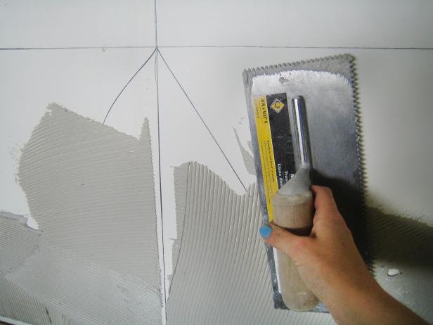 Using a trowel to spread a thin coating of adhesive to a wall.
