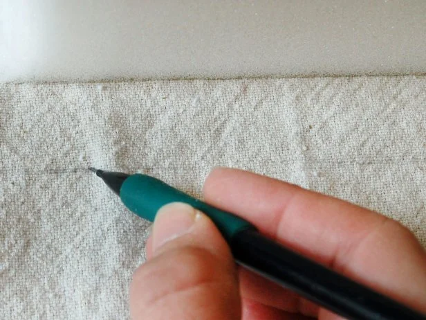 Step 3A in creating a grain sack barstool cushion is to cut the foam cushion. Using the cut foam as a template, trace a line with a pencil for the top and bottom of each cushion, leaving at least a half-inch seam allowance.