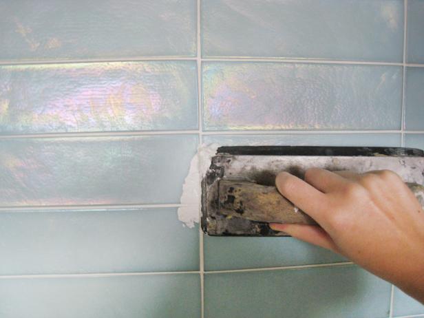 Spreading grout onto a kitchen backsplash with a trowel. 