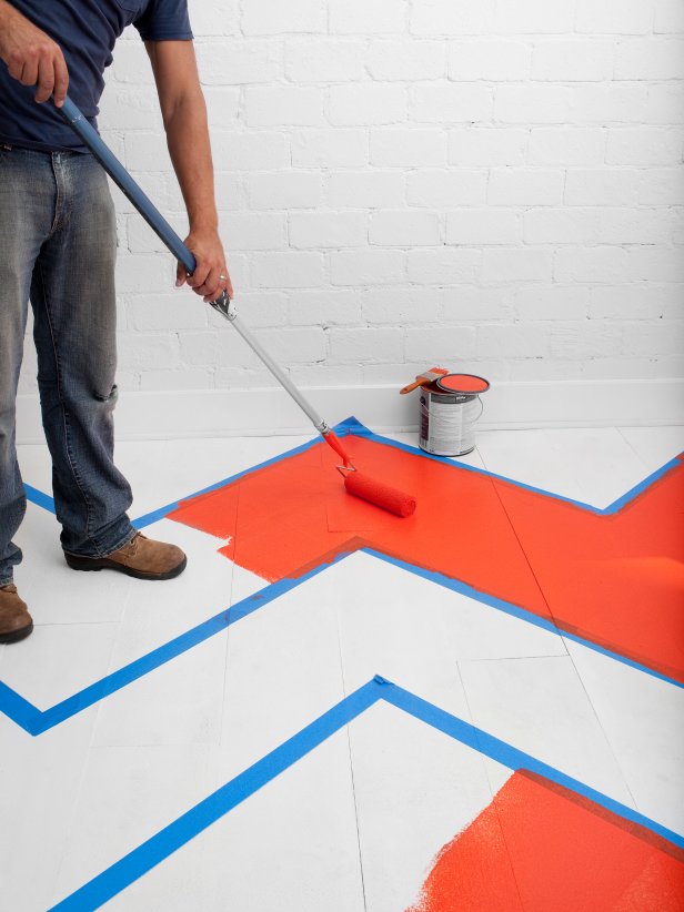 A roller brush  is used to paint red chevron striped on a white floor.
