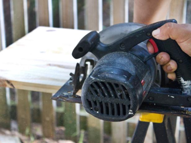 Man using a hand held power saw to cut a piece of lumber lengthwise. 