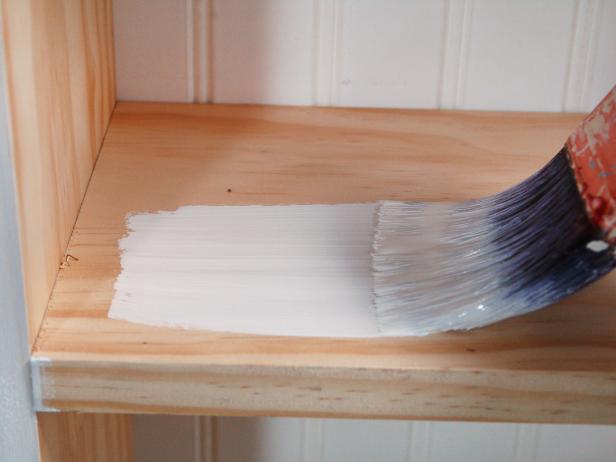 Paintbrush Applying White Paint to Wood Shelf