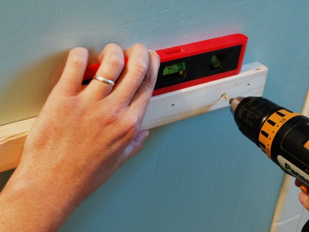 After determining placement of the cabinet, position 1 x 2 board to fit on the wall under the bottom shelf and behind the base molding. Use a level to ensure the shelf will hang straight. Drill pilot holes through the board and wall. Insert screws to hold securely to the wall.