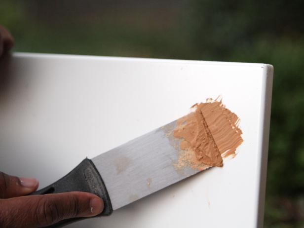 Putty Knife Spreads Wood Filler on White Surface